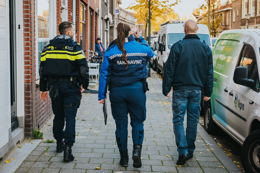 Drie mensen, waarvan een politieagent en een handnaver lopen door de straat