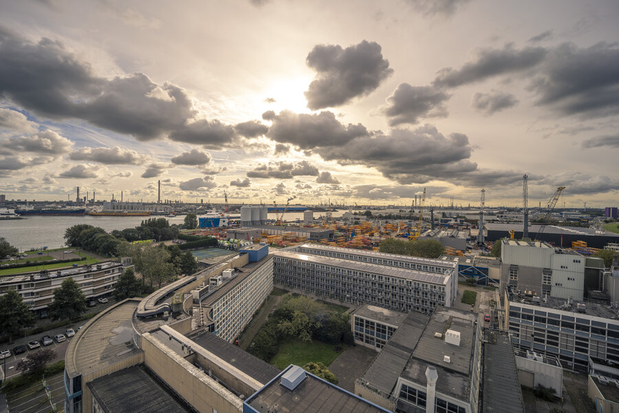 Foto van hoog kijkend over gebouwen richting de Nieuwe Maas en de havens